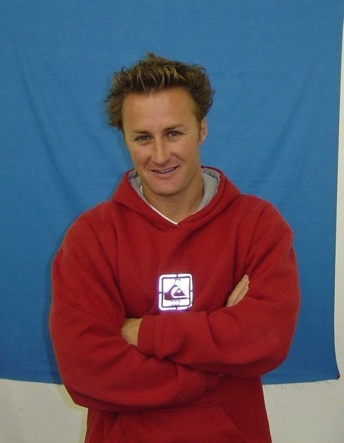 Jason Derek Brown standing and smiling while wearing a red hoodie in blue background