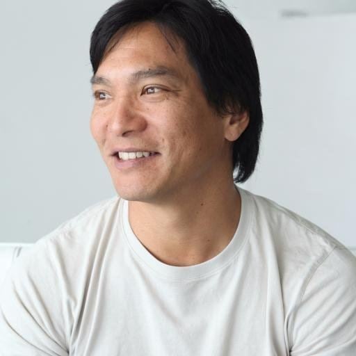Jason Scott Lee smiling while looking afar and wearing a white t-shirt