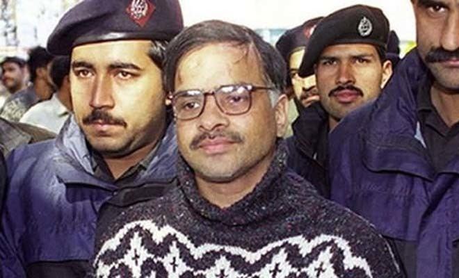 Javed Iqbal accompanied by police officers while wearing a gray and white sweatshirt and eyeglasses