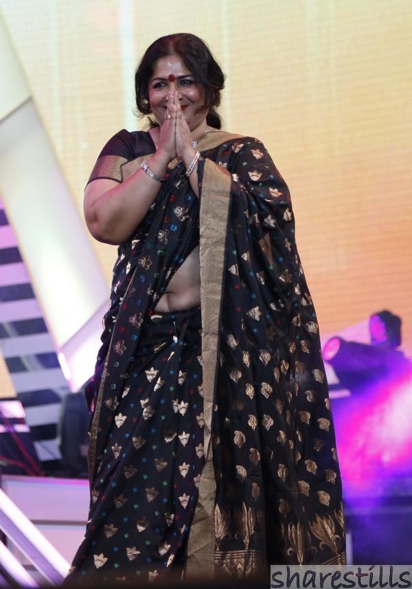 Jayabharathi wearing earrings, rings, bracelets, and a black dress showing her tummy.