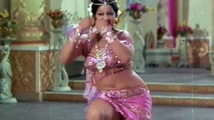 Jayamalini is dancing, wearing many accessories, and a sexy purple top and skirt in a movie scene from Hanthakudi Veta (1987 film).