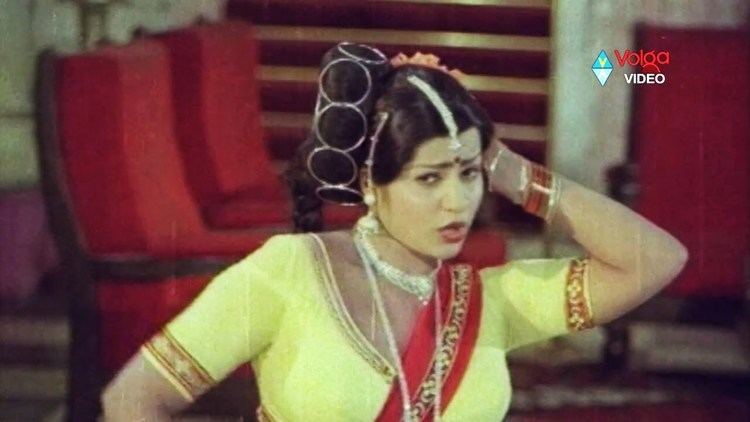 Jayamalini with a seductive facial expression, wearing many accessories, and a yellow and red top in a scene from Hanthakudi Veta (1987 film).