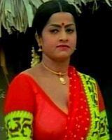 Jayamalini with a serious face, wearing earrings, necklace, and a red and yellow Indian dress.