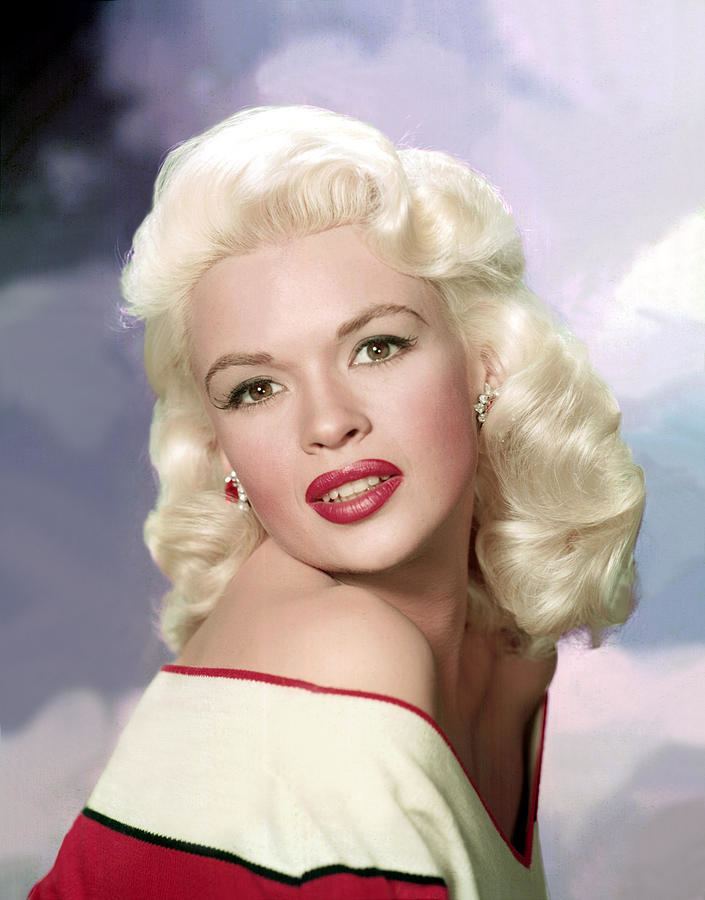 Jayne Mansfield is smiling, has white hair, and wears silver-red earrings and a red-white with black line dress.