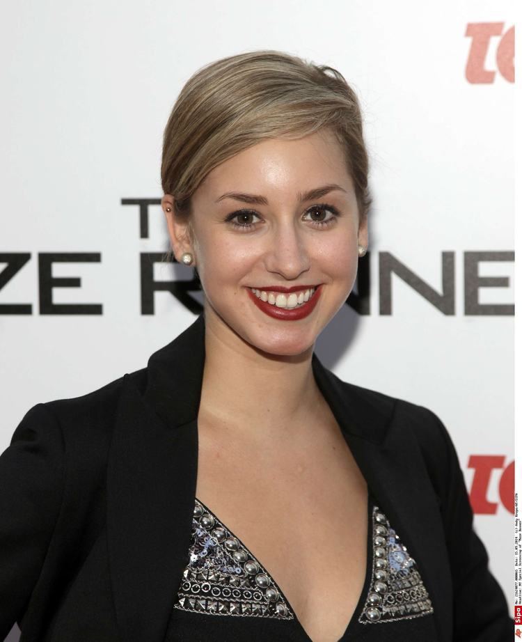 Jazmin Grace Grimaldi smiling while wearing a black coat, black and gray blouse, and earrings