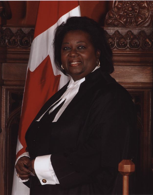 Photo of the Honourable Jean Augustine, standing in front of a Canadian flag