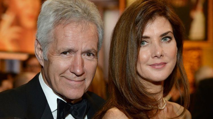 Alex Trebek smiling while wearing a black suit and a bowtie with his wife Jean Currivan Trebek