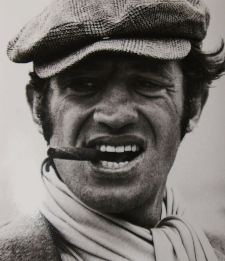 Jean-Paul Belmondo smoking while wearing a cap and scarf