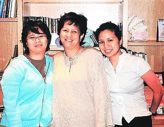 Jeanne Abdullah smiling while wearing a beige blouse and her two daughters Nadiah and Nadene at her side