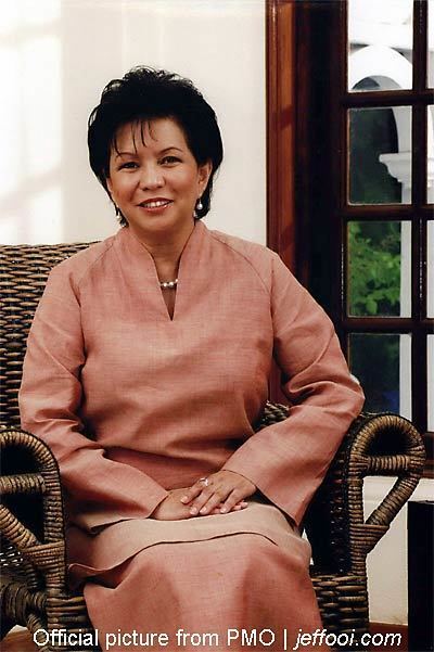 Jeanne Abdullah smiling while sitting on a chair and wearing a brown dress