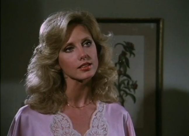 Priscilla Presley as Jenna Wade with wavy hair while wearing a pink blouse and necklace