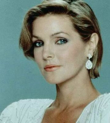 Priscilla Presley as Jenna Wade with a tight-lipped smile while wearing a white blouse and earrings