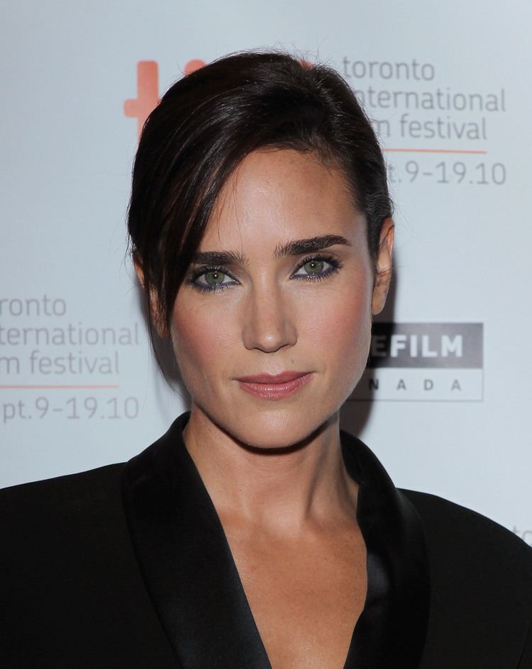 In Toronto International Film Festival Jennifer Connelly is smiling, has long black hair tied up with side bangs, brown eyes and mole on her left upper lips wearing black top.