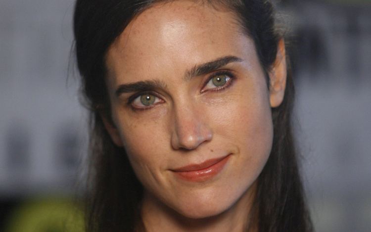 Jennifer Connelly is smiling, has long black hair tied up, brown eyes and mole on her left upper lips.