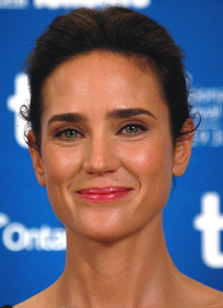 Jennifer Connelly is smiling, has long black hair tied up, brown eyes and mole on her left upper lips.