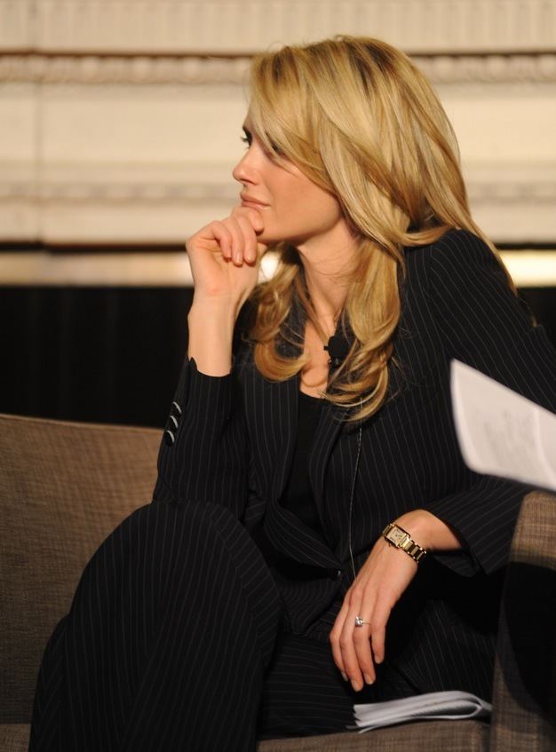 Jennifer Siebel Newsom looking afar while sitting on the couch and wearing a black blazer, black pants, and wristwatch