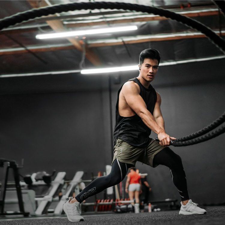 Jeremy Sry holding the battle rope while exercising and wearing a black sando, dark green shorts, black leggings, and white rubber shoes