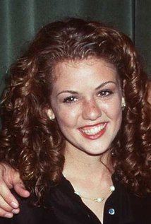 Jessica Bowman smiling with a hand on her shoulder, with curly hair, wearing a necklace, and a black shirt.