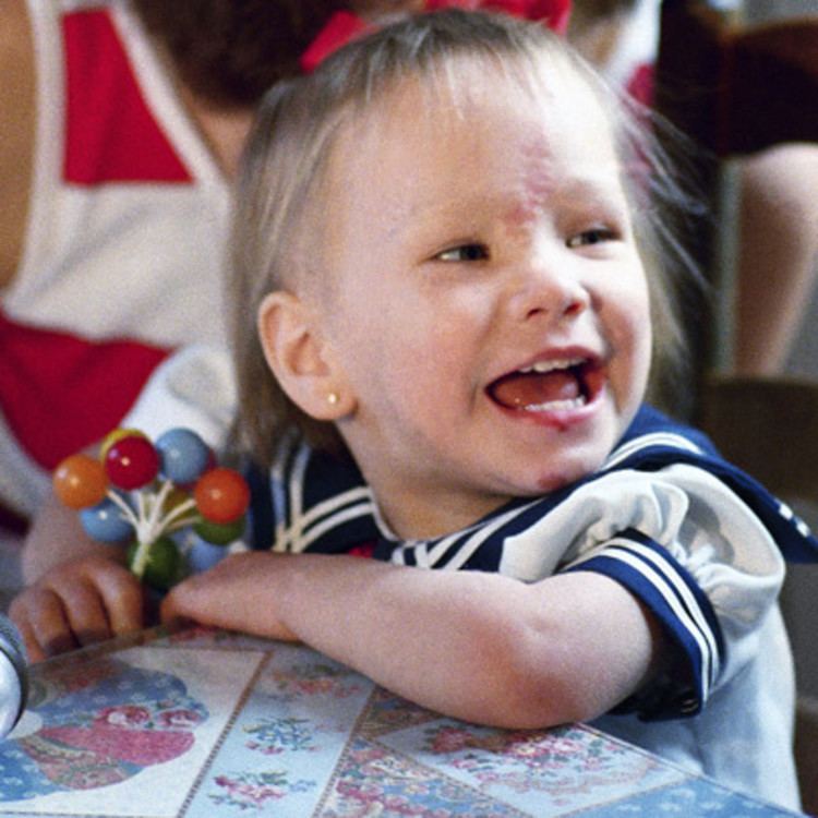 Baby Jessica McClure smiling while wearing white and blue dress