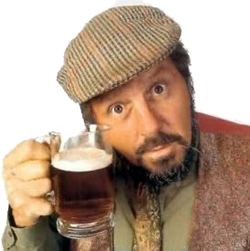 Jethro holding a glass of beer while wearing a beige hat, green long sleeves, maroon vest, and necktie