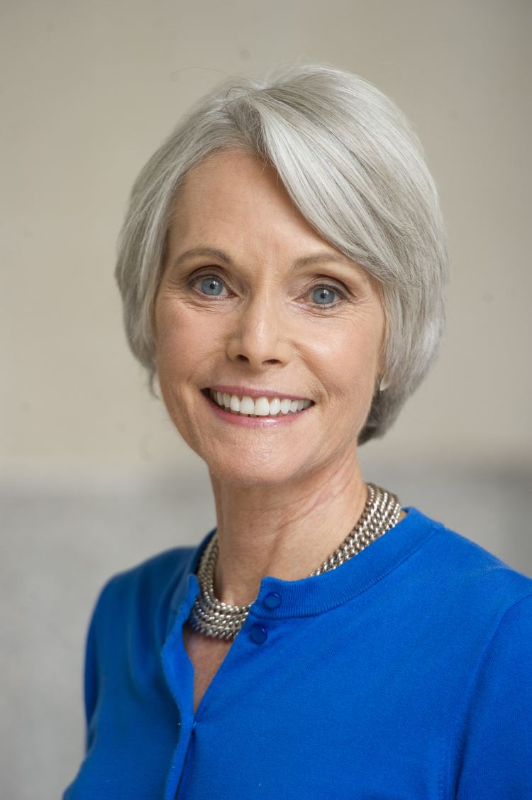 Jill Dougherty smiling with white short hair and wearing a blue blouse and necklace