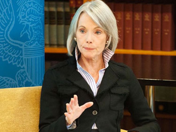 Jill Dougherty speaking during an interview and wearing a gray and white-striped shirt under a black coat