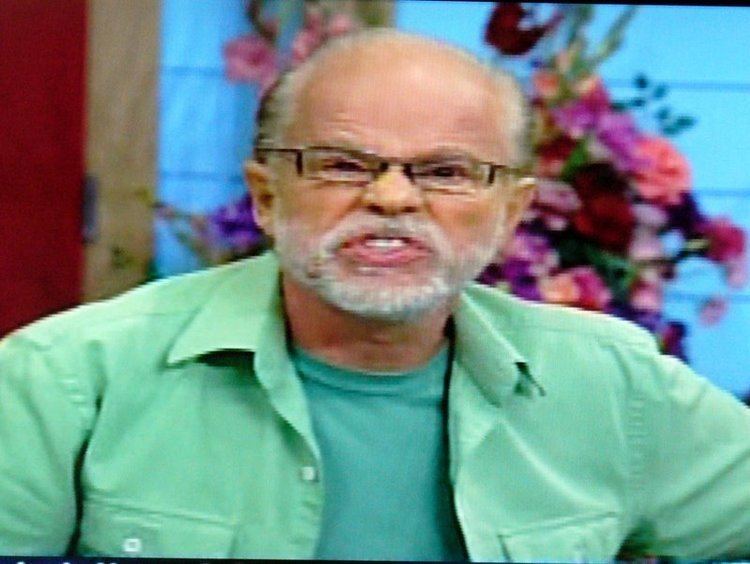 Jim Bakker showing a funny face with a mustache and beard while wearing eyeglasses, a green shirt under a green unbuttoned sleeve