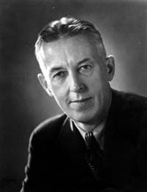 Bill Wilson smiling while wearing a black coat, long sleeves, and necktie