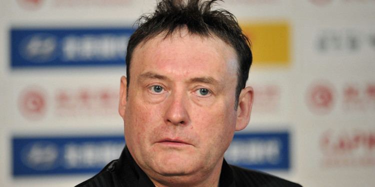 Jimmy White with a serious face, messy hair, and wearing a black vest over black long sleeves.