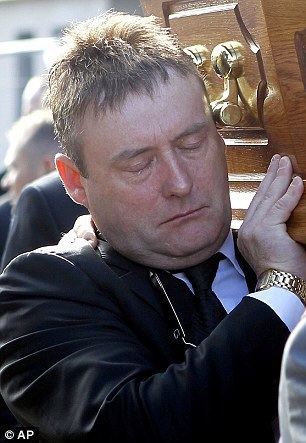 Jimmy White with closed watery eyes while carrying the coffin of Alex Higgins down Belfast's Donegal Road to St Anne's Cathedral. Jimmy wearing a gold watch, a black coat over white long sleeves, and a black necktie.