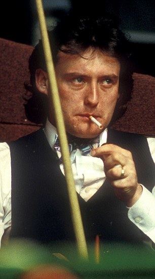 Jimmy White is smoking while holding a cue stick and looking at something, with wavy hair, wearing a black vest over white long sleeves, and a multi-colored bowtie.