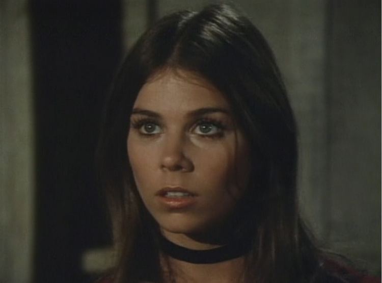 Jo Ann Harris looking at something with darker hair and having a band in her neck.