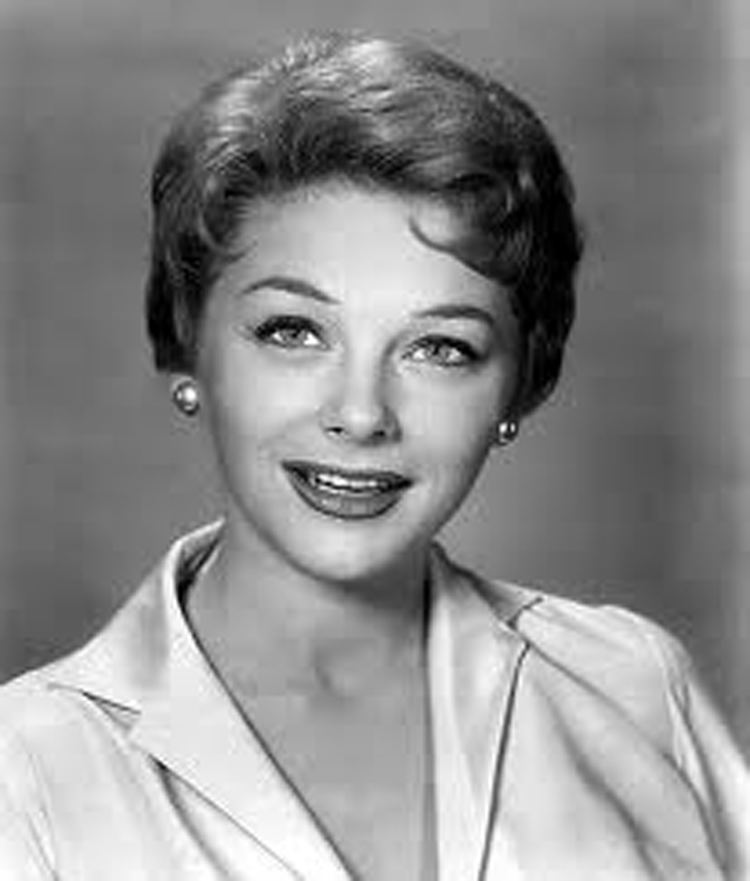 Joanna Moore smiling with short wavy hair while wearing earrings and a blouse with a collar