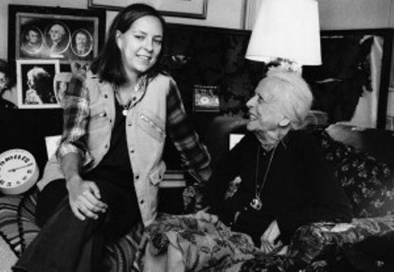 Alice Roosevelt Longworth sitting on a couch with her granddaughter Joanna Sturm sitting in front of her inside their house.