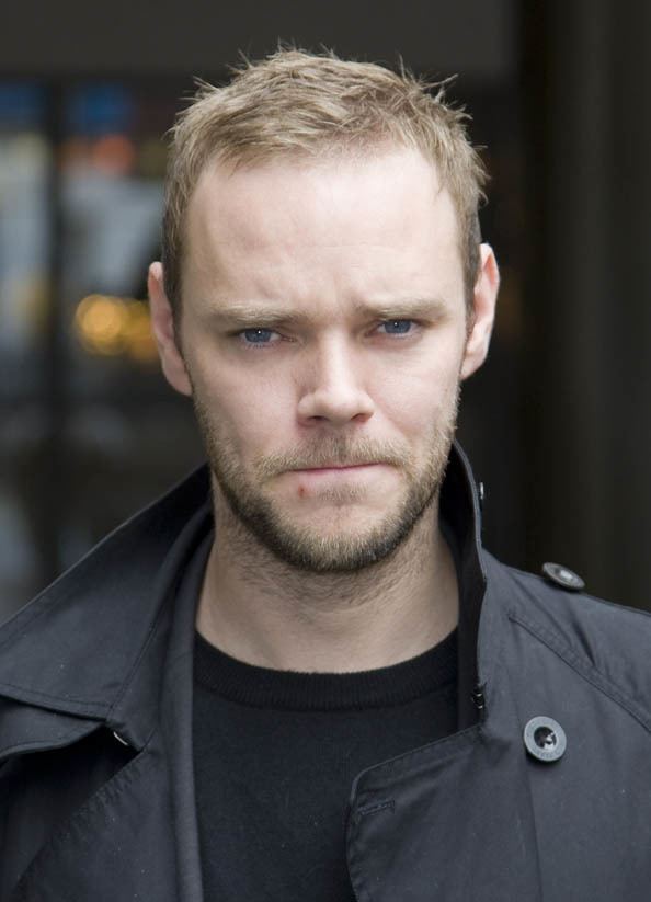 Joe Absolom biting his lips with mustache and beard while wearing a black jacket and black t-shirt