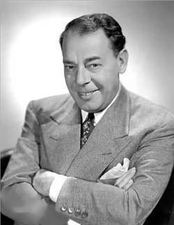 Joe E. Lewis smiling while wearing a coat, long sleeve, and necktie