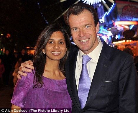 Joel Cadbury smiling and wearing a black coat, white long sleeves, and necktie while Divia Lalvani wearing a violet dress