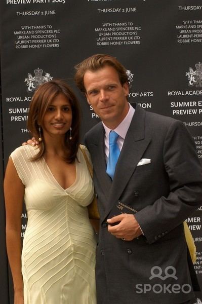 Joel Cadbury wearing a black coat, white long sleeves, and necktie while Divia Lalvani smiling and wearing a cream dress