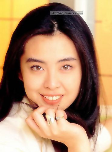 Joey Wong smiling with her hand in her chin and wearing a white blouse and rings on her finger.