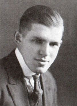 John Augustus Larson with a serious face, wearing a black coat over white long sleeves, and a black necktie.