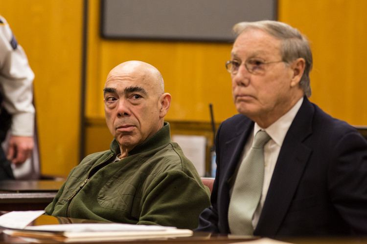 John Cassisi sitting inside a courtroom and wearing a green jacket