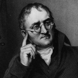 A portrait of John Dalton looking serious with his finger pointing into his head, with eyeglasses wearing a scarf under a black coat