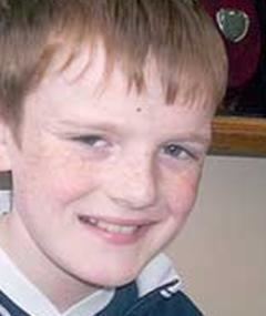 John Joe McNeill smiling while wearing a white and blue t-shirt