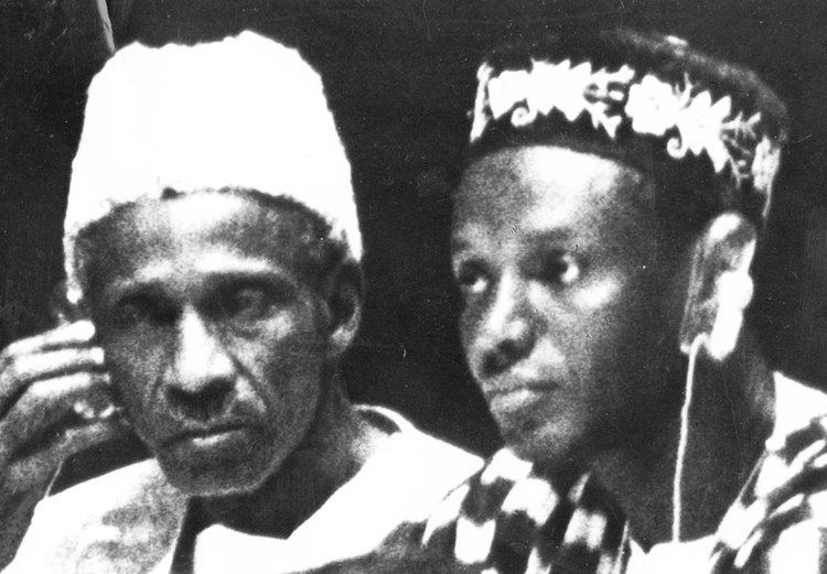 Dr. John Albert Musselman Karefa-Smart, Sierra Leone's first Foreign Minister (left) is serious while holding his right cheek with his right hand, wearing a white Yoruba (in gobi style) and a white Agbada. Milton Augustus Strieby Margai is a Sierra Leonean politician and the first prime minister of West Africa (right) is serious, wearing an earphone in his left ear, a black and white Yoruba (in kufi style with flower design), and a black and white Agbada.