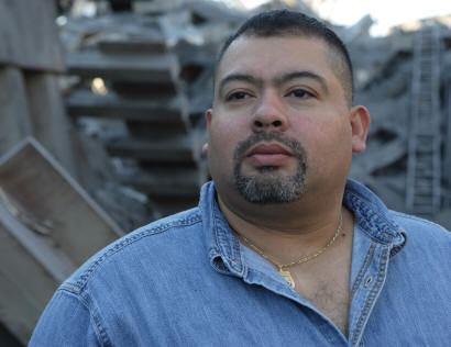 William Jimeno looking afar, with mustache and beard, and wearing a denim polo and necklace