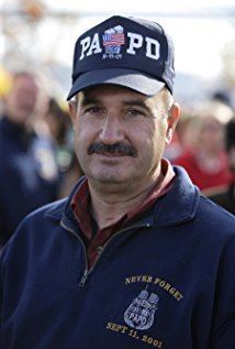 John McLoughlin with a tight-lipped smile and mustache and wearing the PAPD dark blue cap, brown long sleeves, and dark blue jacket