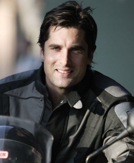 John Newton (actor) smiles while holding his helmet wearing a black jacket