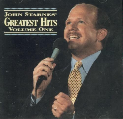 John Starnes wearing a black coat, blue long sleeves and red and yellow neck tie on his Greatest Hits Volume 1