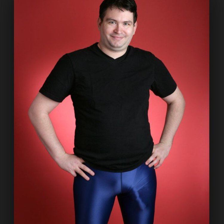 Jonah Falcon wearing black t-shirt and blue leggings while smiling and hands on his hips