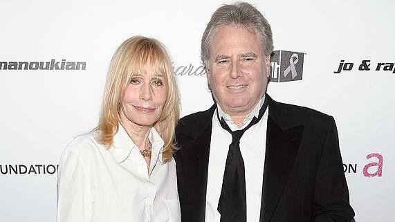 Jonathan D. Krane smiling while Sally Kellerman with a tight-lipped smile. Jonathan is wearing a black coat over white long sleeves and a black necktie while Sally with blonde hair, wearing a necklace and a white long sleeve top.
